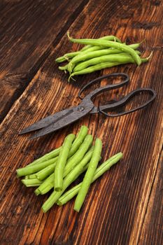 Raw fresh green beans with water drops on brown wooden textured table. Fresh vegetable eating. 