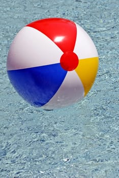 Colorful big beach ball floating in sparkling water in swimming pool
