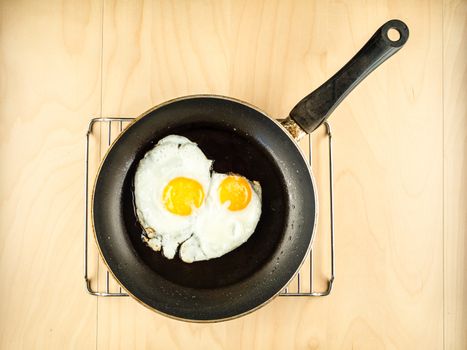 Two fresh fried eggs on the black pan, wooden kitchen table, simple top view, minimal composition with copy space