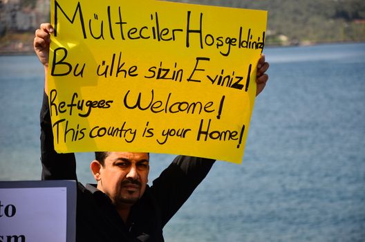 TURKEY, Dikili: A man holds a sign reading Refugees welcome! This country is your home! as migrants who are deported from Lesbos and Chios islands in Greece to Turkey, arrive on April 4, 2016 in the port of Dikili, in Izmir district. Migrants return from Greece to Turkey begun under the terms of an EU deal that has worried aid groups, as Athens struggles to manage the overload of desperate people on its soil. Over 51,000 refugees and migrants seeking to reach northern Europe are stuck in Greece, after Balkan states sealed their borders. Hundreds more continue to land on the Greek islands every day despite the EU deal.