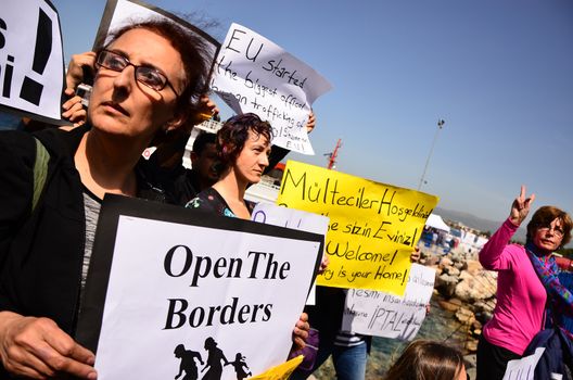 TURKEY, Dikili: A woman holds a sign reading Open the borders as migrants who are deported from Lesbos and Chios islands in Greece to Turkey, arrive on April 4, 2016 in the port of Dikili, in Izmir district. Migrants return from Greece to Turkey begun under the terms of an EU deal that has worried aid groups, as Athens struggles to manage the overload of desperate people on its soil. Over 51,000 refugees and migrants seeking to reach northern Europe are stuck in Greece, after Balkan states sealed their borders. Hundreds more continue to land on the Greek islands every day despite the EU deal.