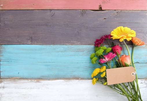 Bunch of flowers with blank gift label on wooden background