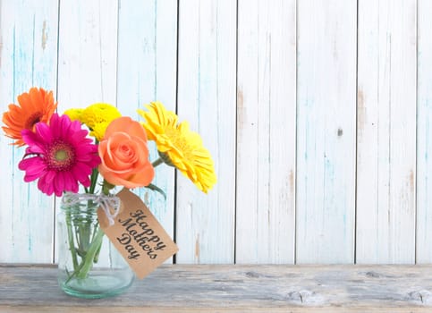 Mixed variety of flowers in a glass jar over a white background with gift tag 