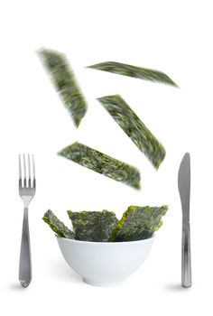 Seaweed slices falling into a bowl over a white background, a superfood that is high in vitamin c, iron and promotes healthy bacteria in the gut 