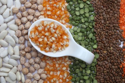 Ceramic spoon with corn seeds over seeds and grains background