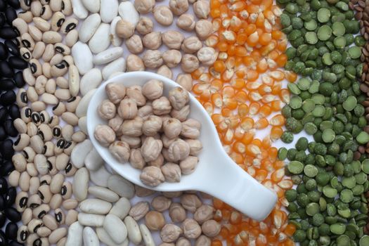 Ceramic spoon with chickpeas over seeds and grains background