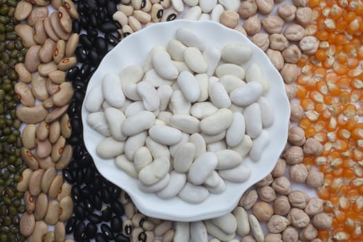 Ceramic plate with white beans over seeds and grains background