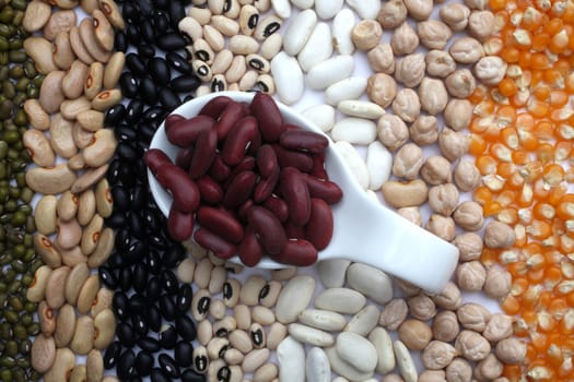 Ceramic spoon with red beans over seeds and grains background