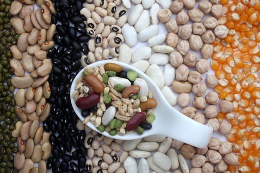 Ceramic spoon with mixed beans over seeds and grains background