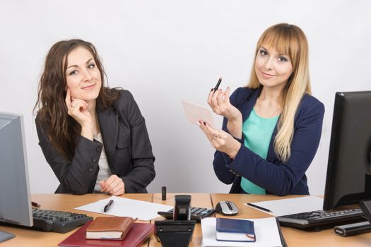 Office employee watches as a colleague is going to make up lips at the desk