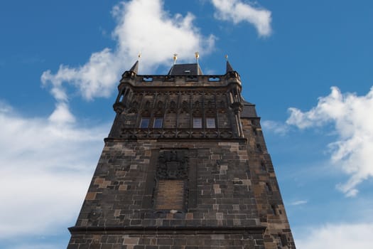 Close up detailed historical gothic stone tower view in Prague, on cloudy blue sky background.