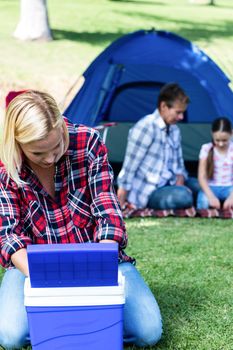 Woman looking into the cool box outside a tent and family sitting in background