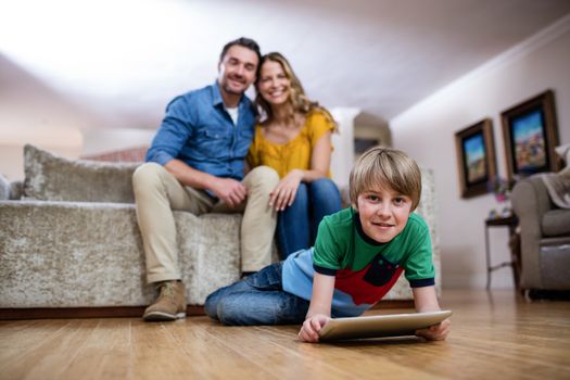Boy using a digital tablet while parents sitting on sofa in background at home