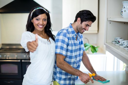 Woman showing her thumbs up while man cleaning the kitchen at home