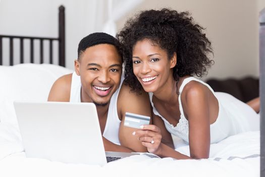 Happy couple shopping online through laptop using credit card in bedroom