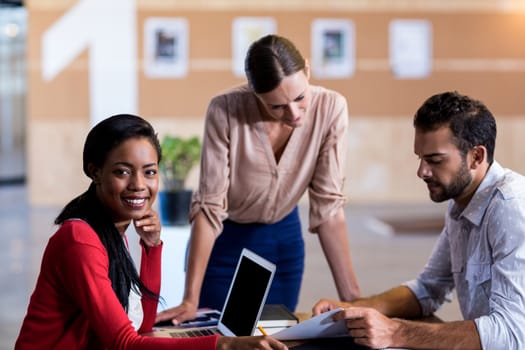 Team of colleagues discussing at their desk while a colleague smiling at camera