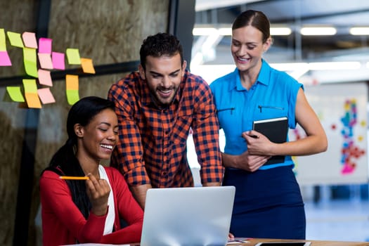 Colleagues interact using laptop at their desk in the office