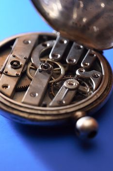 Old pocket watch back side with open mechanism on blue background