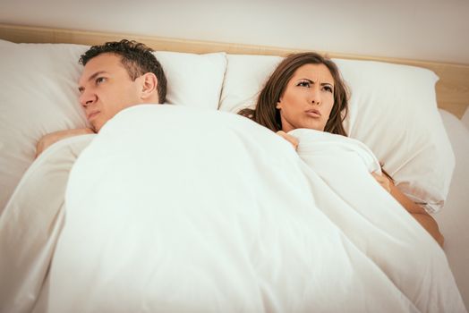 Young couple laying in bed with an expression of anger and displeased on their faces.