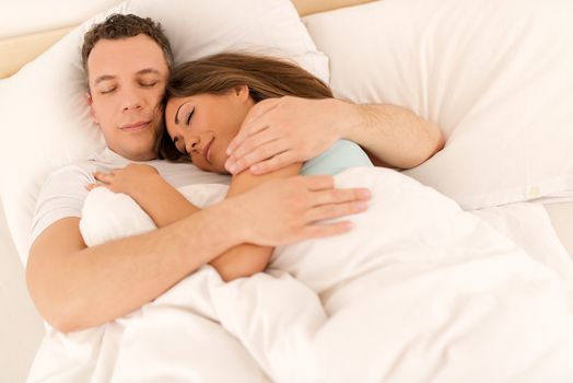 Beautiful young loving couple hugging sleeping in bed. 