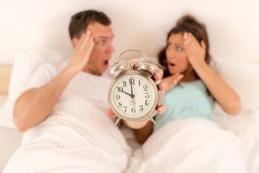 Young couple in bed awaken to the ringing of the alarm clock. They is late in the morning. Focus on the alarm clock, on the foreground.