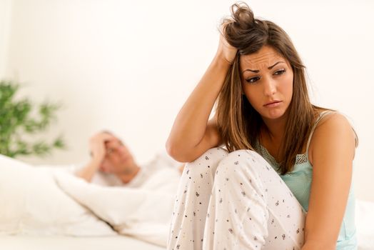 Young worried woman sitting on the bed because of relationship difficulties.