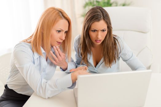 Two young worried businesswoman looking on laptop in the office.