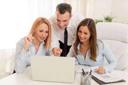 Three smiling colleagues working at laptop in the office