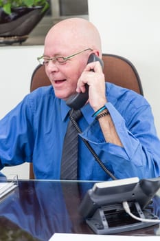 Happy casual businessman at desk on phone taking notes