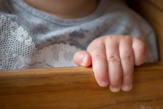 Hand of a baby girl holding onto the side of her chair