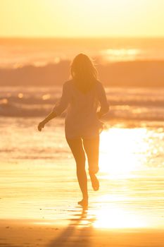 Happy woman enjoying isummer, running joyfully on beach in sunset.