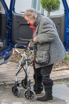Elderly lady with a walker in front of a car.