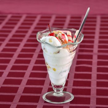 Great ice cream with berries, and assorted fillers in a glass. Stands on a table covered with a checkered red tablecloth.