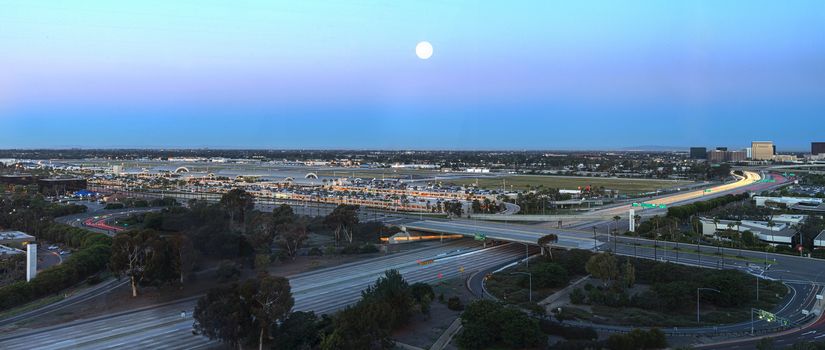 Aerial view of John Wayne Airport in Orange County, California, at sunrise with light trails across the 405 highway in front.