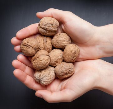 hands holding handful of walnuts over wooden table