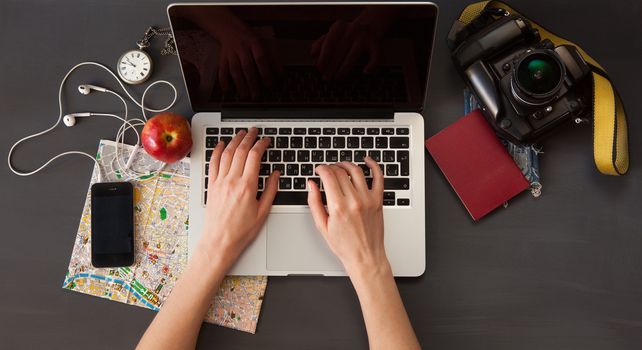 Outfit of the traveler. The view from the top. young woman sitting at the vintage brown wooden table. there are the map, camera, passport, watch, laptop and mobile phone with headphones on the table 