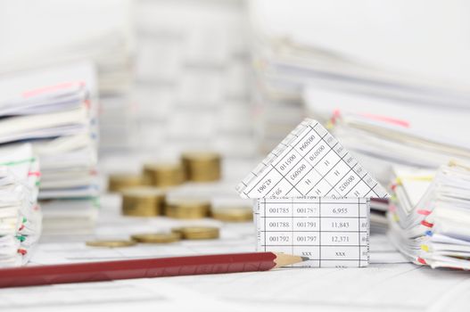 House and brown pencil on finance account have blur step pile of gold coins between overload of paperwork with colorful paperclip as background.