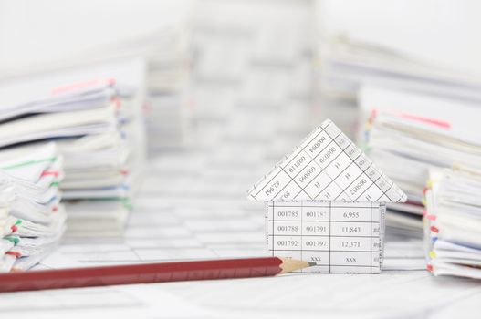 House with pencil on finance account between blur overload of paperwork with colorful paperclip as background.