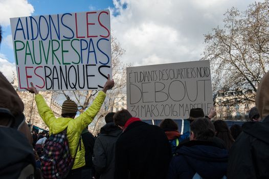 FRANCE, Paris: A protester holds a sign reading Help the poor not the banks as thousand militants of the Nuit debout (Standing night) movement gather on April 7, 2016 at the Place de la Republique in Paris, as participants plan to spend the night camped out to protest against the government's planned labour reform and against forced evictions. It has been one week that hundred of people have occupied the square to show, at first, their opposition to the labour reforms in the wake of the nationwide demonstration which took place on March 31, 2016.