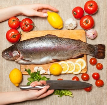 Female hand with a kitchen knife. Fresh trout with vegetables  on cutting board.