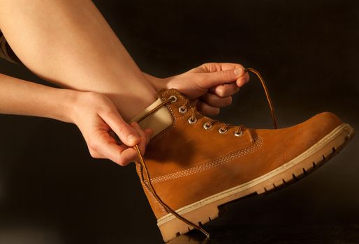 young woman hiker tying shoelaces yellow shoes. dark background