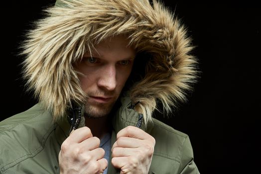 Low key studio portrait of young adult caucasian model wearing winter coat with hood on. Isolated on black.