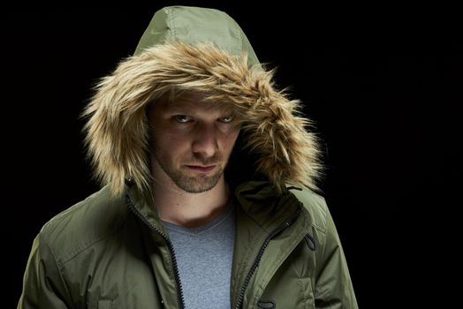 Low key studio portrait of suspicious young adult caucasian model wearing winter coat with hood on.