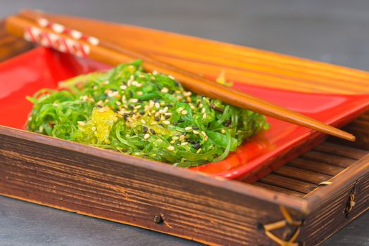 Fresh seaweed salad on a red plate in a bamboo server.
