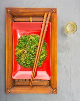 Fresh seaweed salad on a red plate with chopsticks.