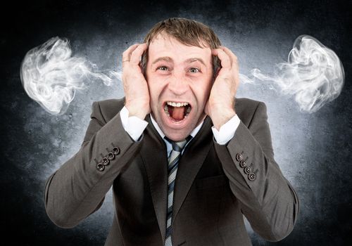 Screaming businessman looking at camera with smoke from his ears on grey wall background