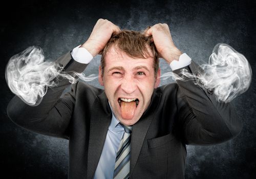 Businessman tearing his hair and with smoke from his ears on grey wall background