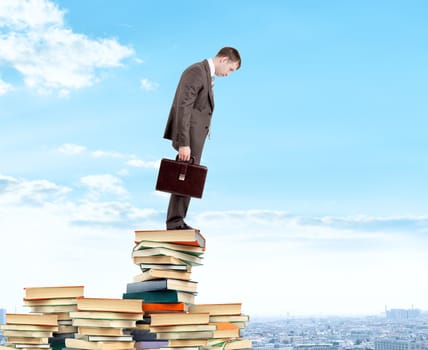 Businessman looking down from piles of books above city