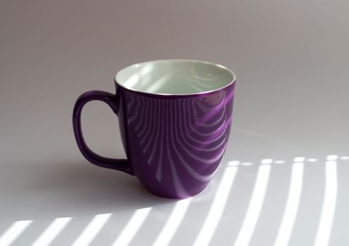 cup on a white table with shadows from the blinds incident