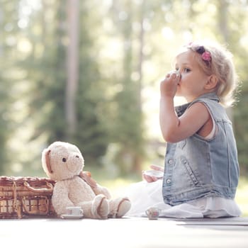 Pretty girl playing with teddy bear outdoors